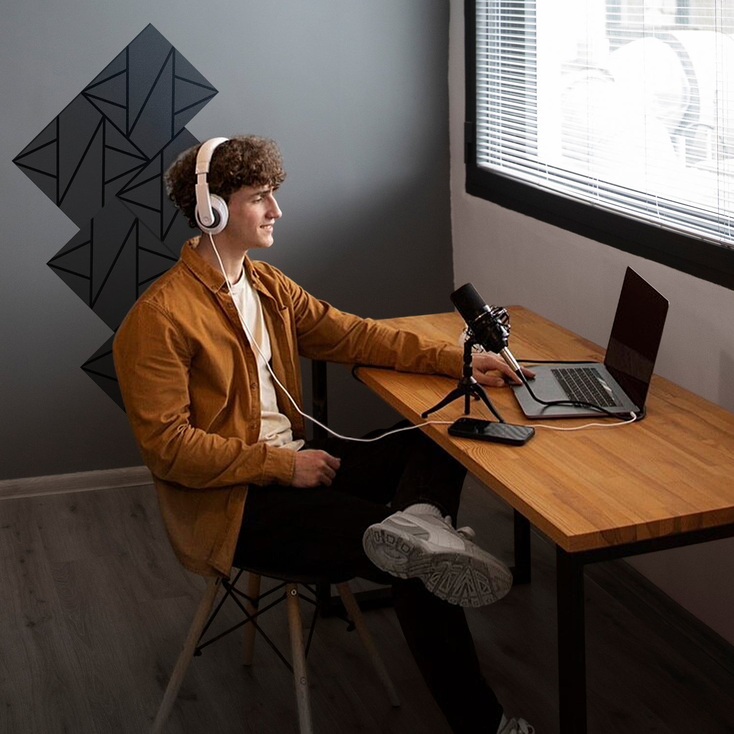 Person sitting at a desk with a laptop and microphone, wearing headphones in a room with geometric xpneuma acoustic panels  wall art.